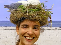  3. Platz: Die Möwenflüsterin, fröhliches Mädchen mit einem Möwennest mit Möwe auf dem Kopf am Strand