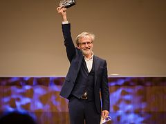  Jörn Sturm, Geschäftsführer der Hinz&Kunzt gGmbH, trägt einen schwarzen Anzug und hält den Metropolitaner Award in die Luft.