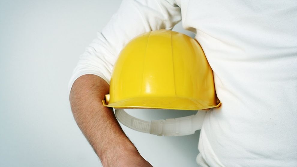  Ein Mensch trägt einen gelben Helm unter dem Arm.