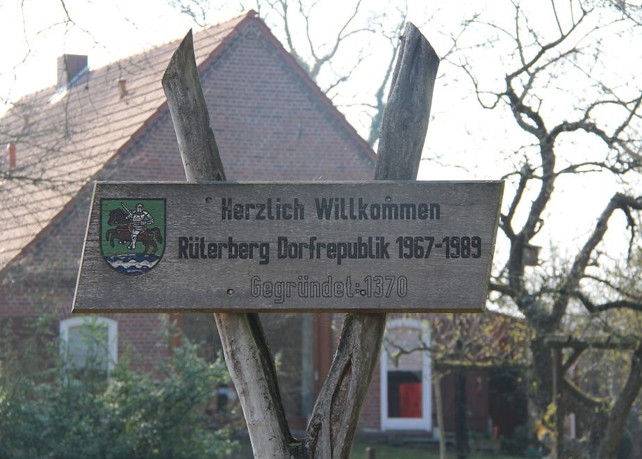 Holzschild auf dem "Herzlich Willkommen Rüterberg Dorfrepublik" steht
