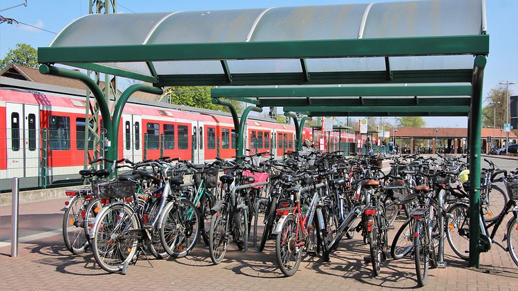  Fahrräder an einer Bike and Ride-Station vor einem Zug