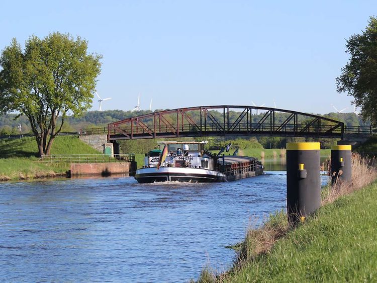  Auf einem Kanal fährt ein Schiff unter einer Brücke hindurch.