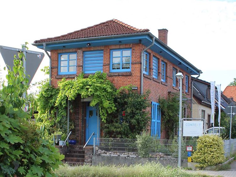 Ein Haus mit blauen Fensterrahmen und Türen steht an einer Kreuzung.