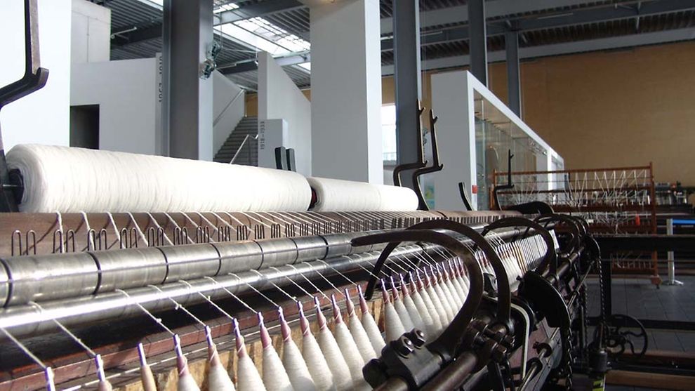 In Einer Maschine sind Wollfäden einspannt. Es ist eine Maschine im Museum Tuch + Technik in Neumünster.