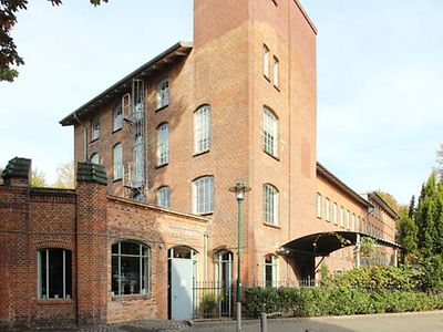  Die hemalige Papierfabrik ist ein rotes Backsteingebäude mit hohen Fenstern. Ein Teil des Gebäudes ist ein rechteckiger Turm, der andere Teile überragt.