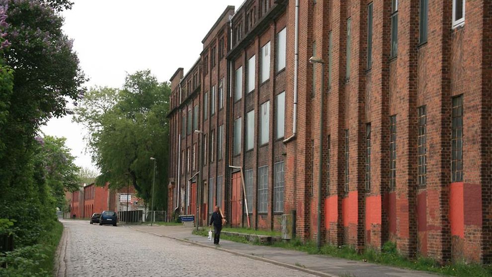 An der Seite einer Kopfsteinpflasterstraße steht ein Gebäude aus rotem Backstein.