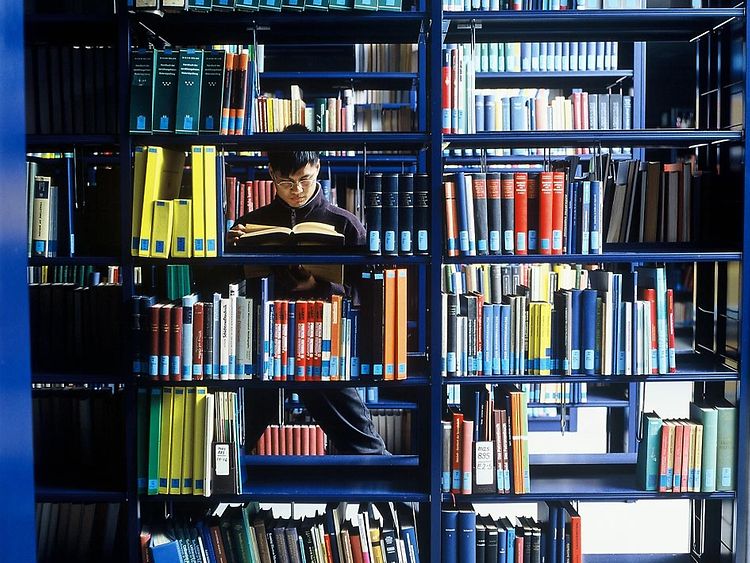  Student hinter Bücherregal in einer Bibliothek